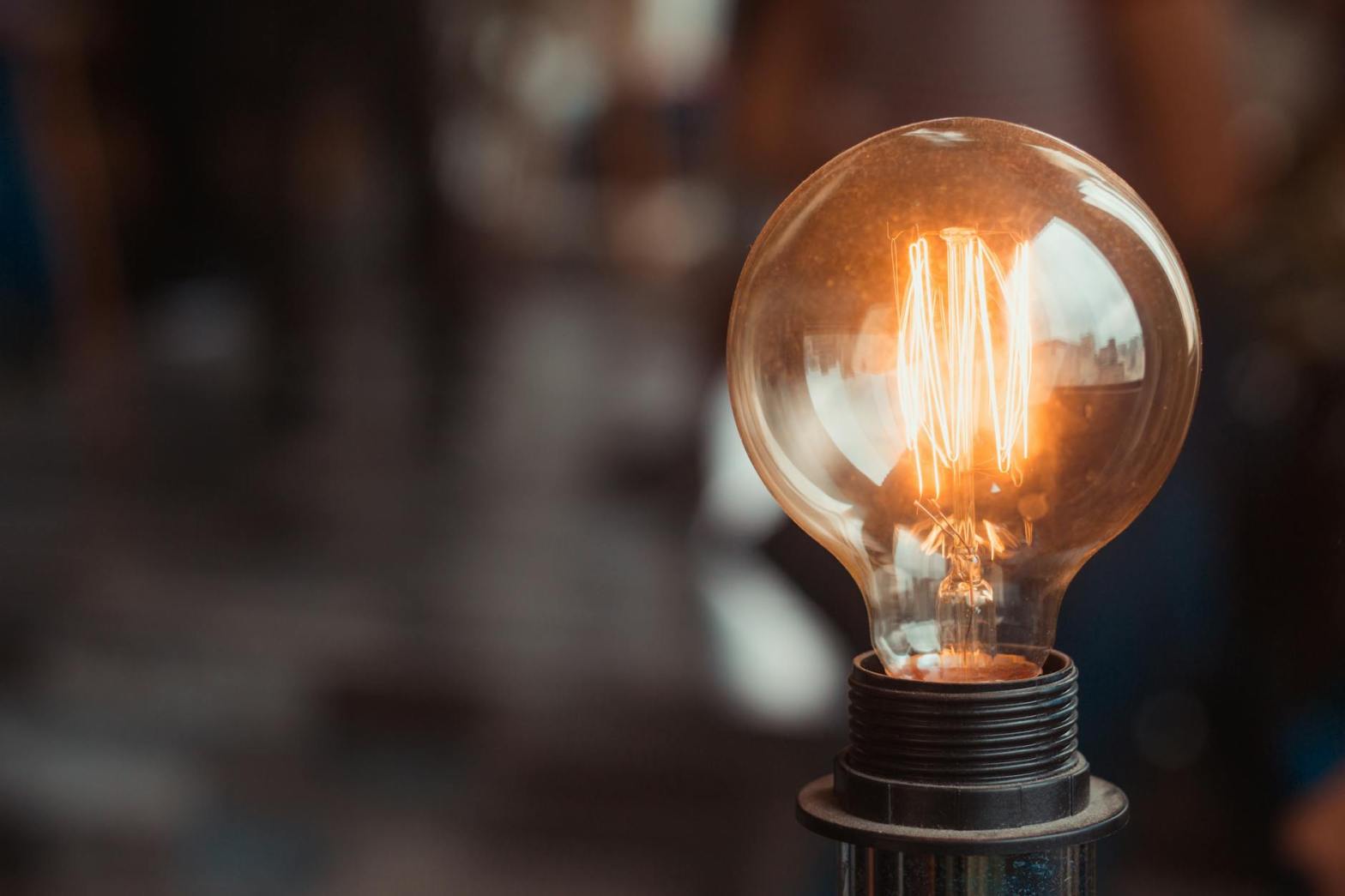 Close-up of a glowing vintage-style light bulb with visible filament, set against a softly blurred background.